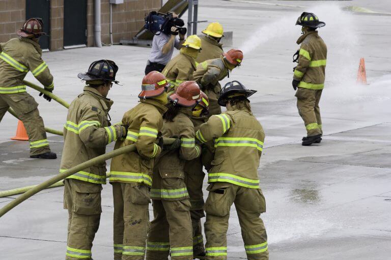 Firefighters in training, learning to handle the firehose. Notice the cameraman in the background.