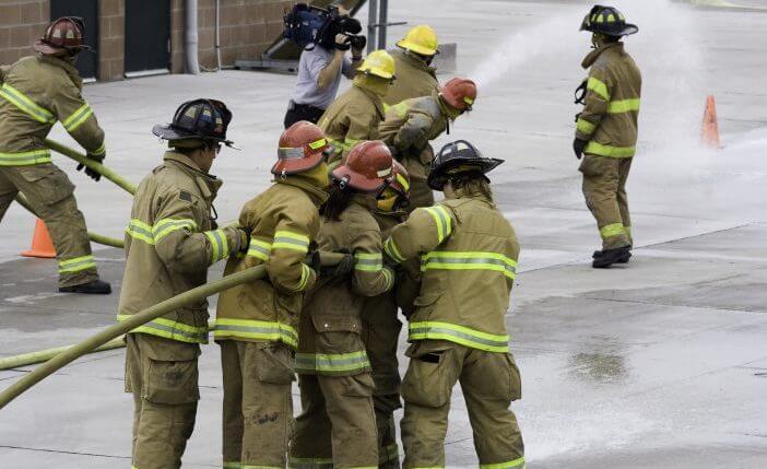 Firefighters in training, learning to handle the firehose. Notice the cameraman in the background.