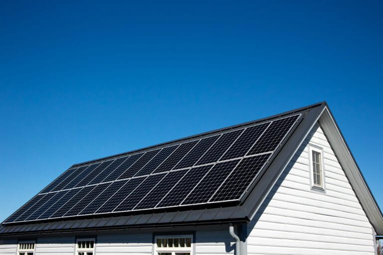 Solar panels on small wood board domestic house roof, sustainable energy concept. Lot of copy space on clear blue sky.