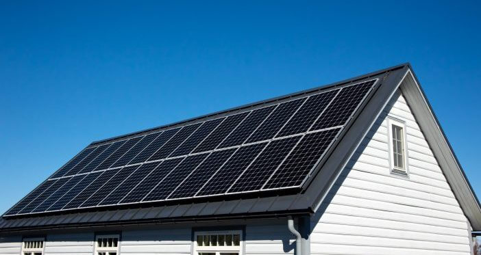 Solar panels on small wood board domestic house roof, sustainable energy concept. Lot of copy space on clear blue sky.