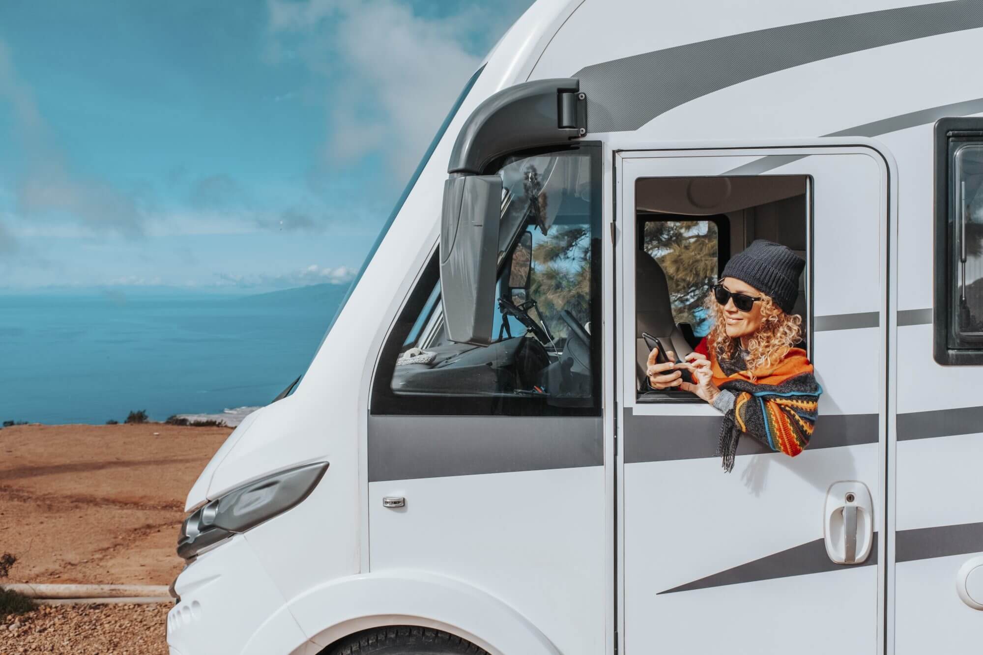 One woman enjoy arrival vacation travel destination after drive a big camper van motor home. Concept of happy female people in van life lifestyle. Summer journey. Planning road trip on mobile phone