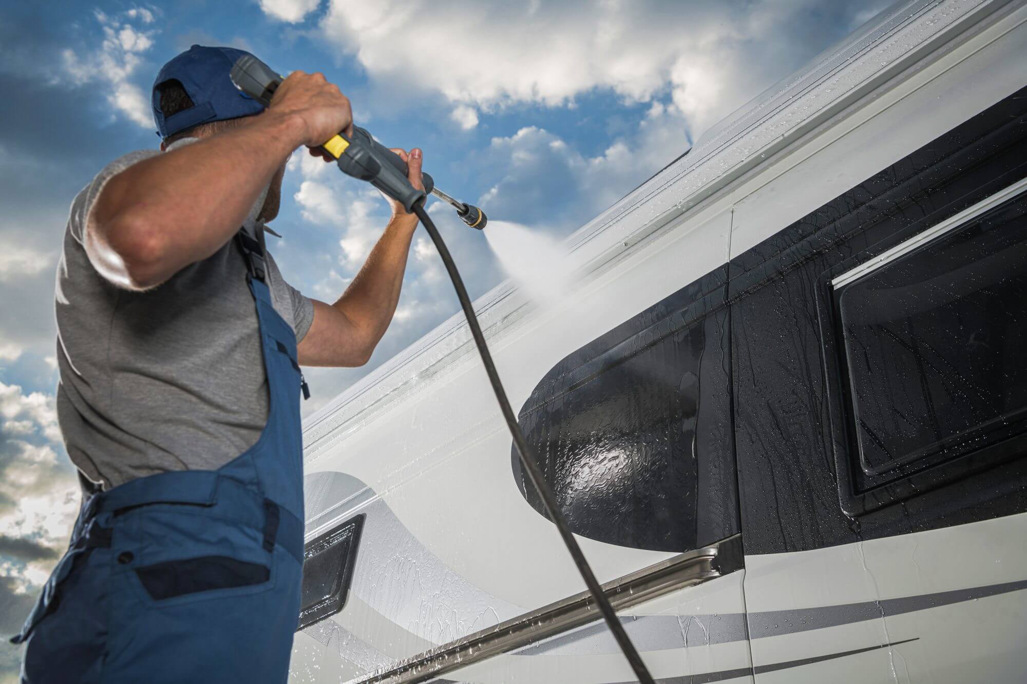 Caucasian Men Pressure Washing His Modern Camper Van RV Class B. Recreational Vehicle Maintenance. Keeping Motorhome Clean.