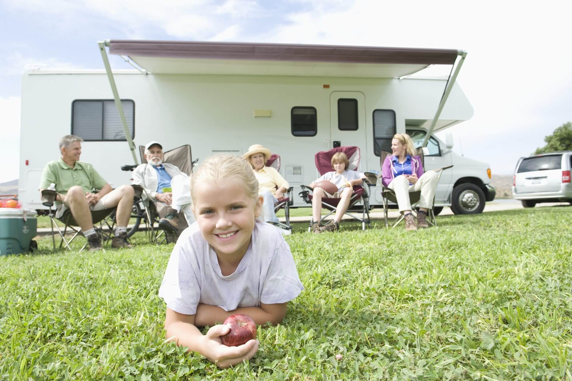 Portrait of a cute little girl lying on grass with family sitting outside RV home