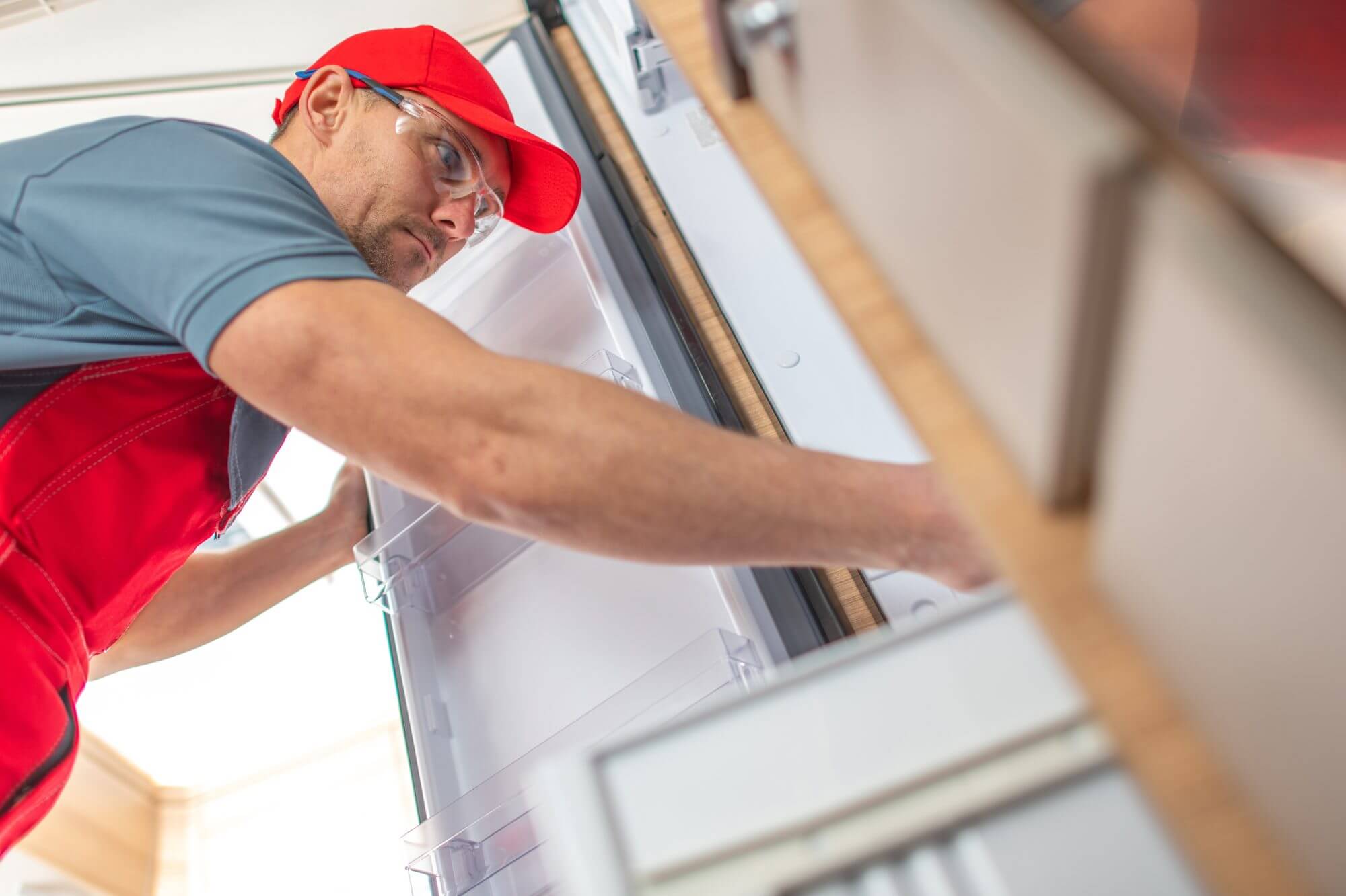 Caucasian RV Appliances Technician Looking Inside Camper Refrigerator Looking For Potential Problem. Recreational Vehicles Maintenance Theme.