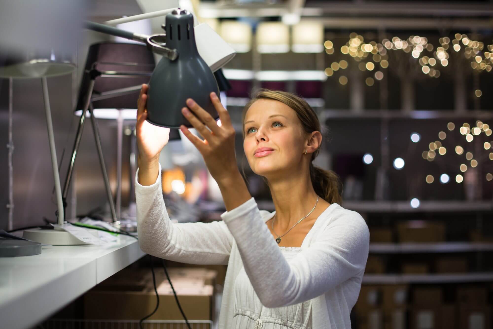 Pretty, young woman choosing the right light for her apartment in a modern home furnishings store (color toned image; shallow DOF)
