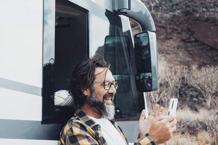 Happy tourist with camper van use mobile phone to call and speak remote friends with voice and internet connection in the country side. Roaming online technology and travel lifestyle people