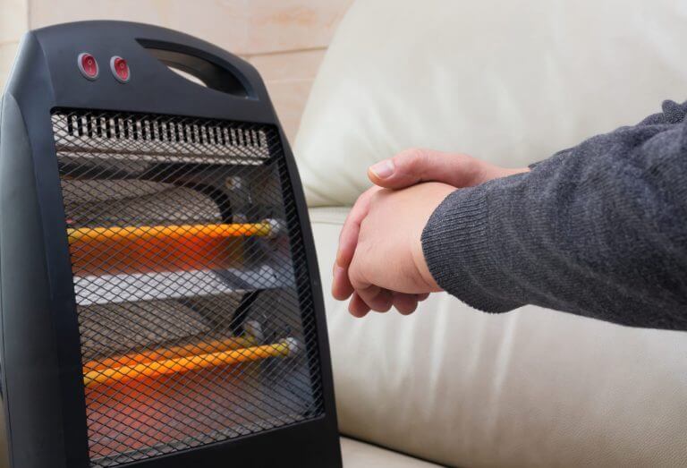 man sitting on sofa with an electric heater near his hands