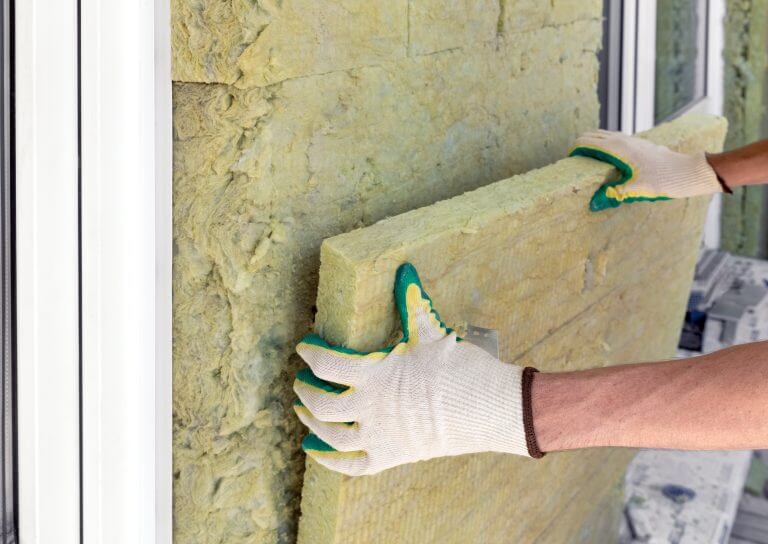 Builder insulates the external walls with mineral sheet insulation in protective gloves. Thermal insulation work, house renovation.