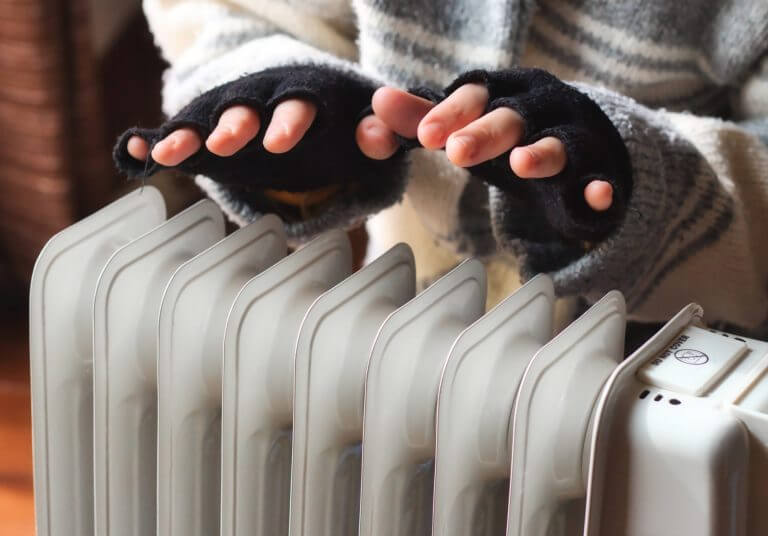 Person heating their hands at home over a domestic portable radiator in winter