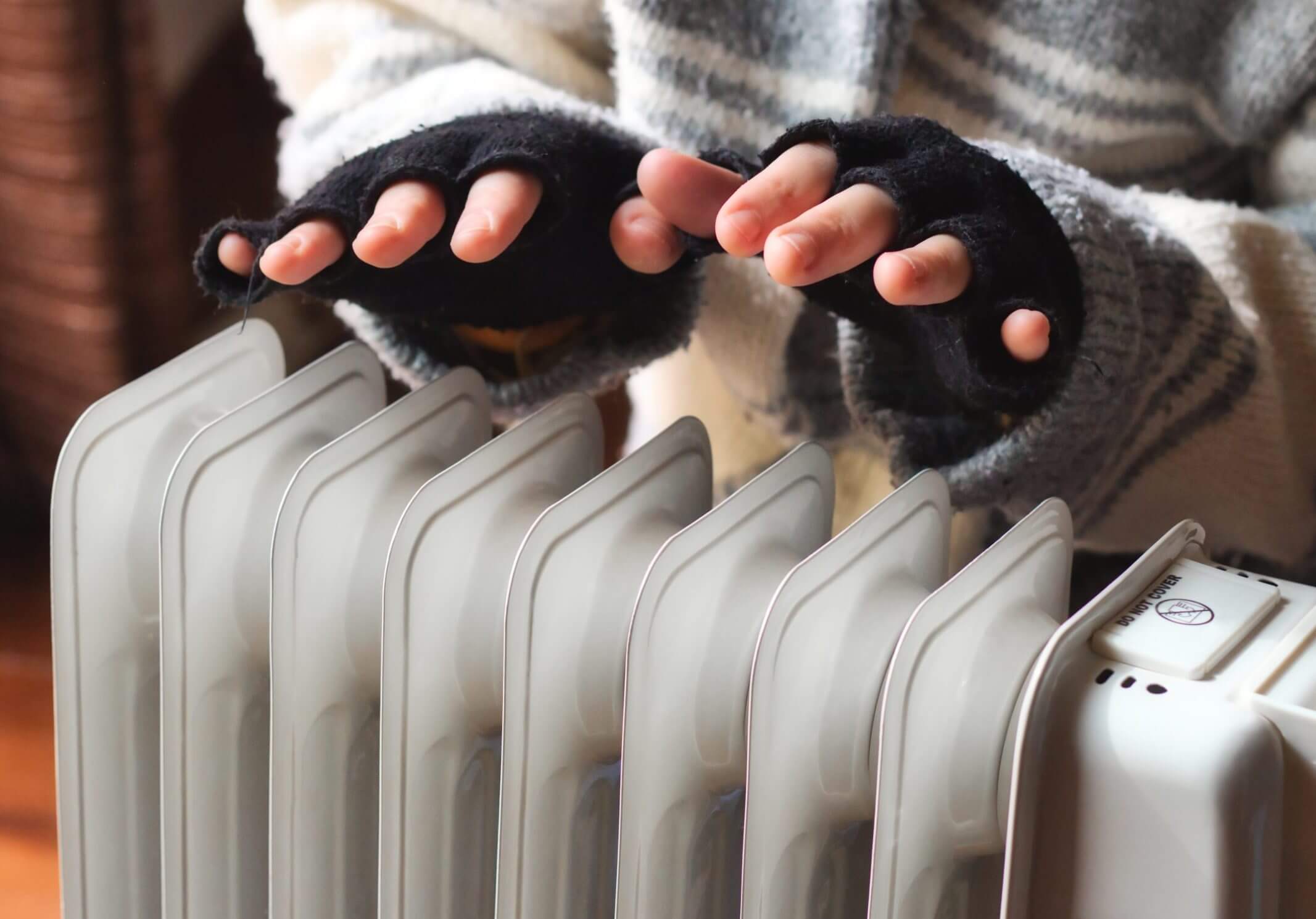 Person heating their hands at home over a domestic portable radiator in winter