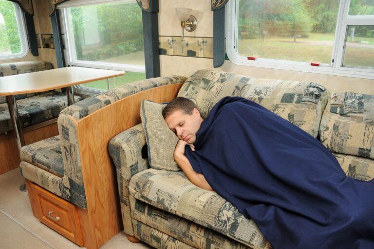 Man sleeping on couch in recreational vehicle.