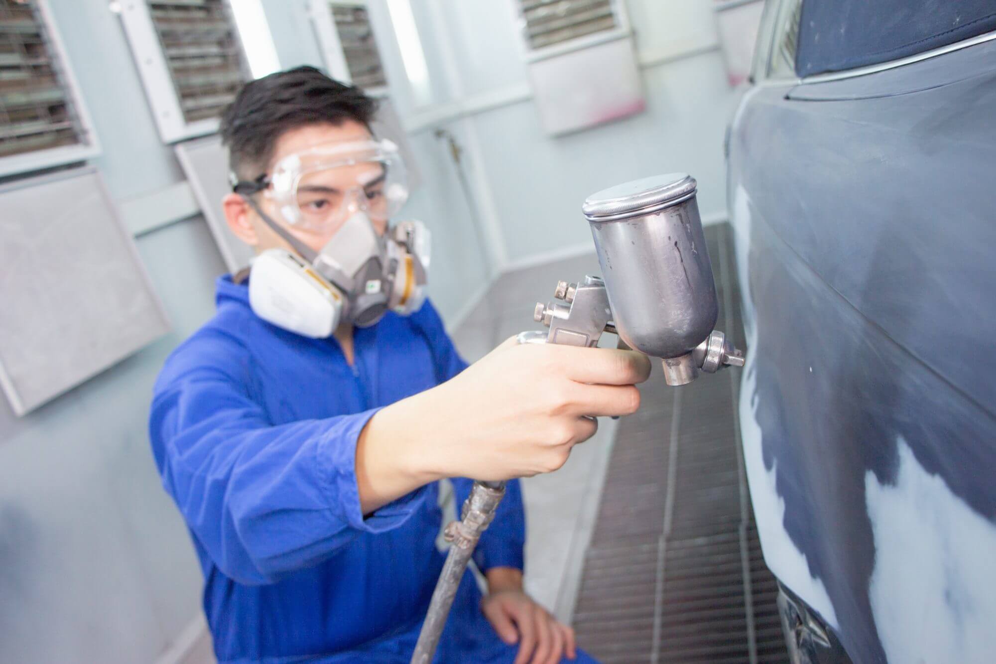 entrepreneur businessman small business owner, paint garage, car repair shop.Painter worker wearing jumpsuit and dust mask holding a spray gun in the paint room.