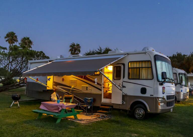 Motor home at a Rv park with lights on around the Rv with a evening sky