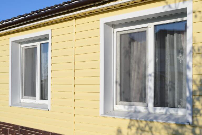 The wall of a private house with plastic  windows covered with yellow vinyl siding