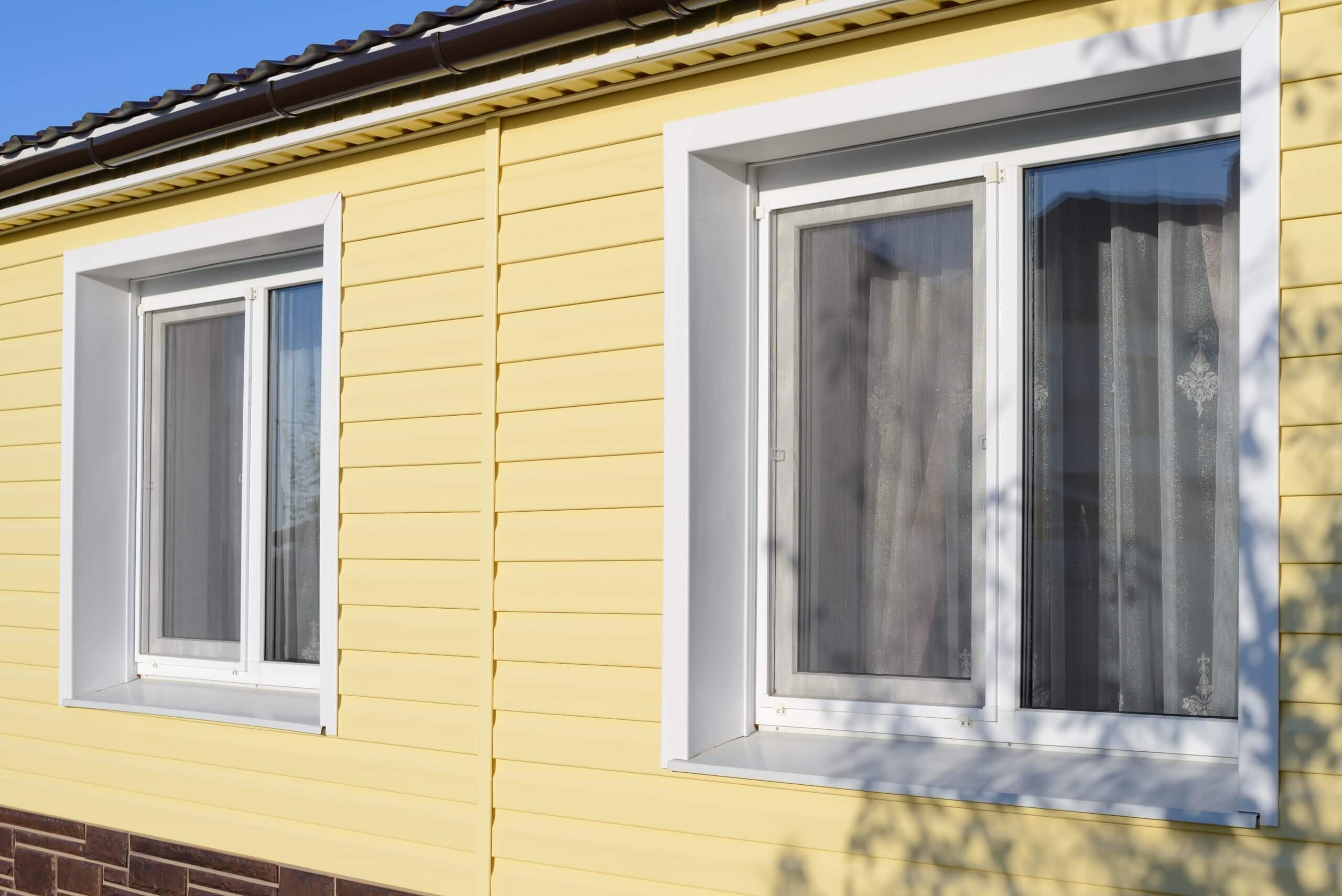 The wall of a private house with plastic  windows covered with yellow vinyl siding