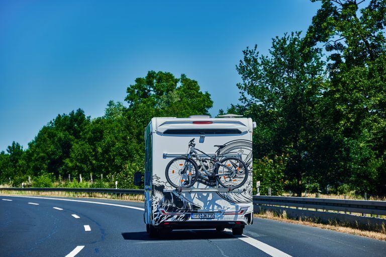 Brandenburg, Germany - June 21, 2022: Camper with a bike carrier attached to the stern and a bicycle mounted on it on a country road.