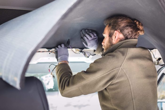 A man is putting insulation on the inside of a van. Conversion of a transporter into a camper van.