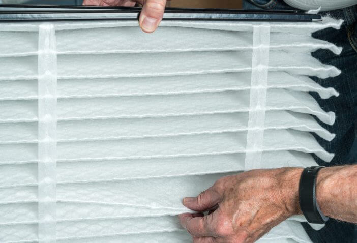 Senior caucasian man checking a clean folded air filter in the HVAC furnace system in basement of home