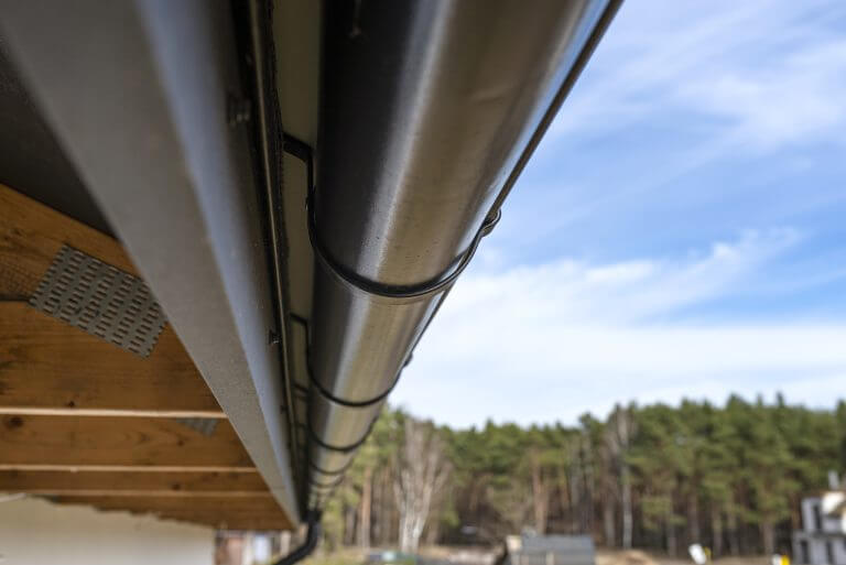 A metal, black gutter on a roof covered with ceramic tiles in the background a forest, bottom view.