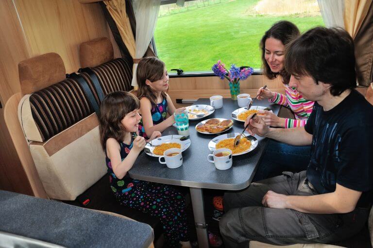 Family eating together in RV interior, travel in motorhome (camper, caravan) on vacation