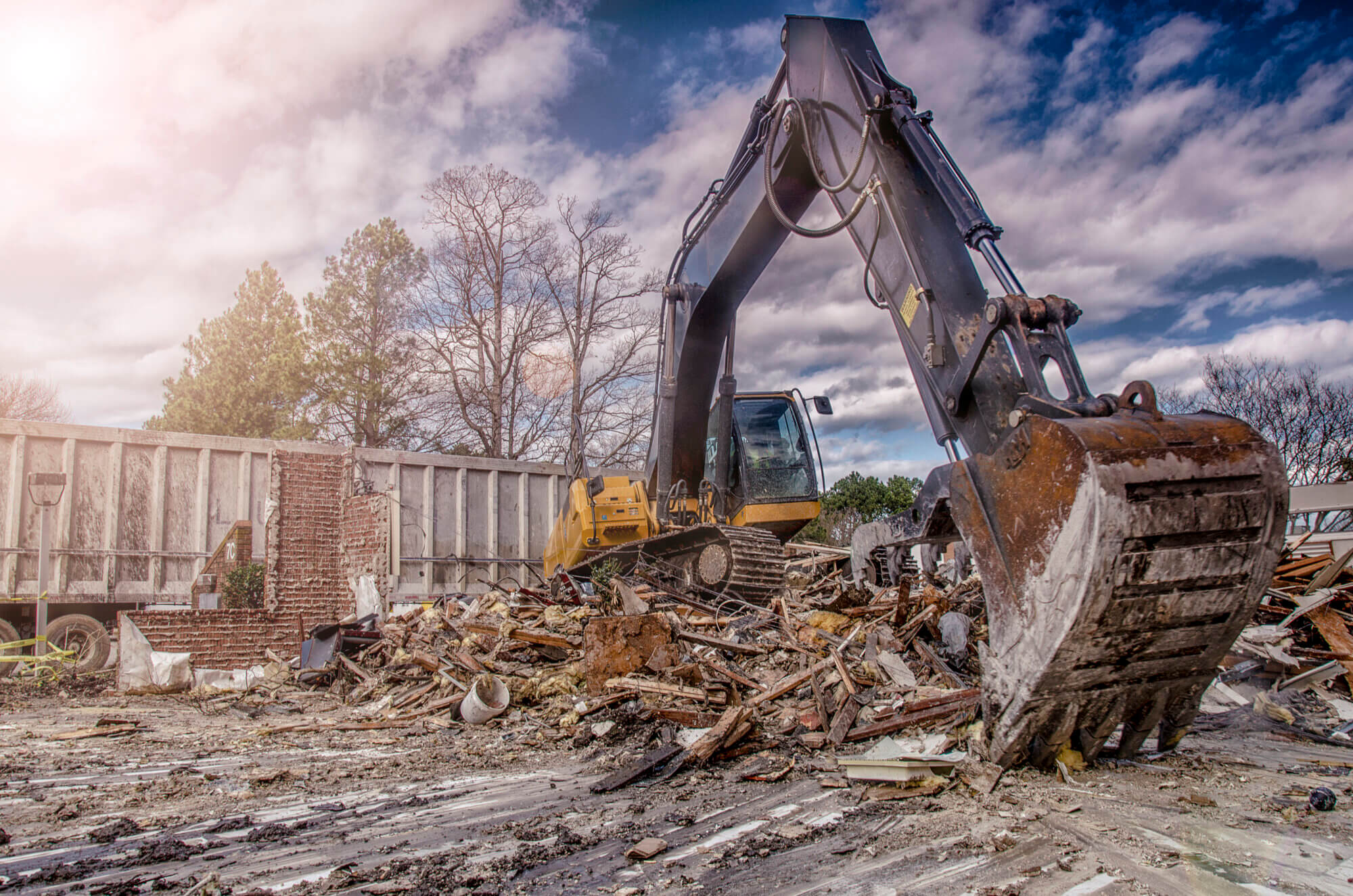 An excavator cleans debris at a construction site while the sun sets with a blue sky.