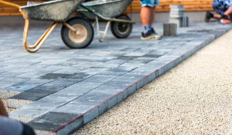 Laying gray concrete paving slabs in house courtyard driveway patio. Professional workers bricklayers are installing new tiles or slabs for driveway, sidewalk or patio on leveled 
foundation base made of sand at public or private residence.
