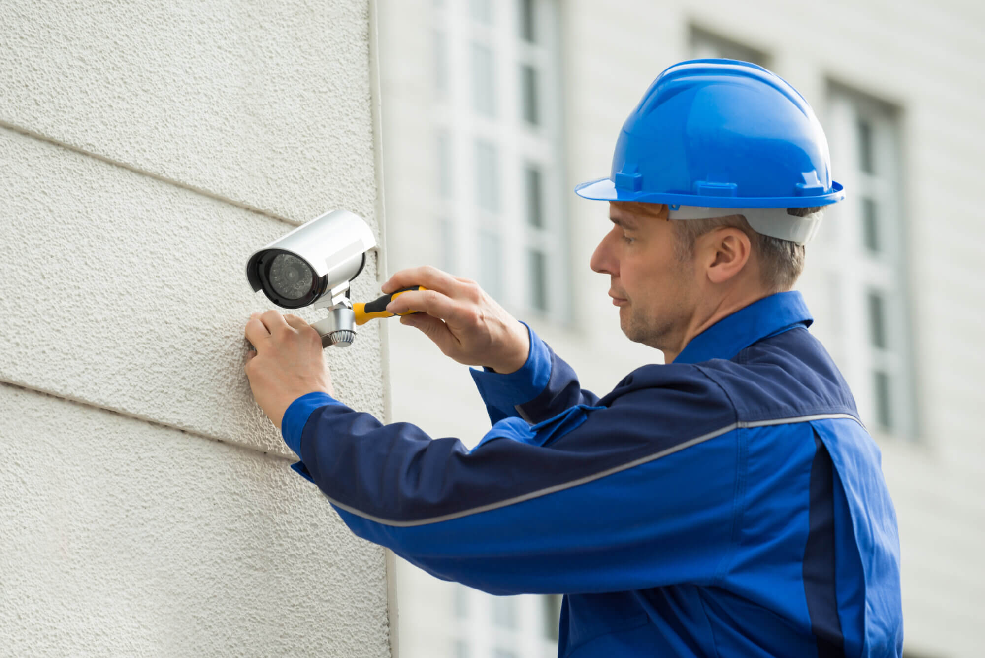 Mature Male Technician Installing Camera On Wall With Screwdriver