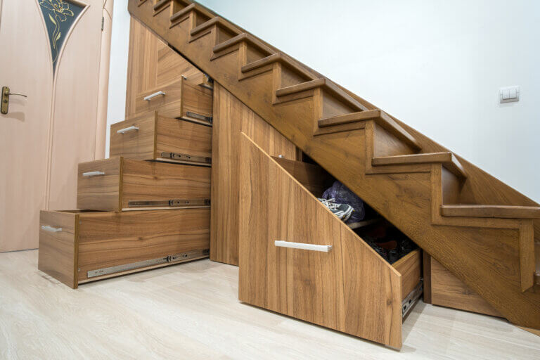 Modern architecture interior with luxury hallway with glossy wooden stairs in multi-storey house. Custom built pullout cabinets on glides in slots under stairs. Use of space for storage.