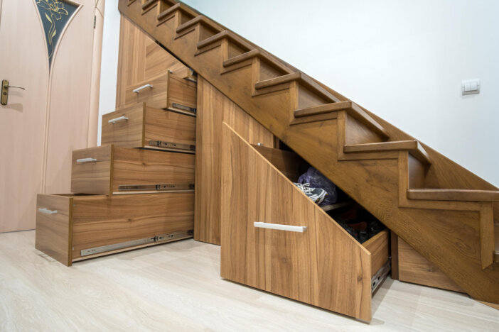 Modern architecture interior with luxury hallway with glossy wooden stairs in multi-storey house. Custom built pullout cabinets on glides in slots under stairs. Use of space for storage.
