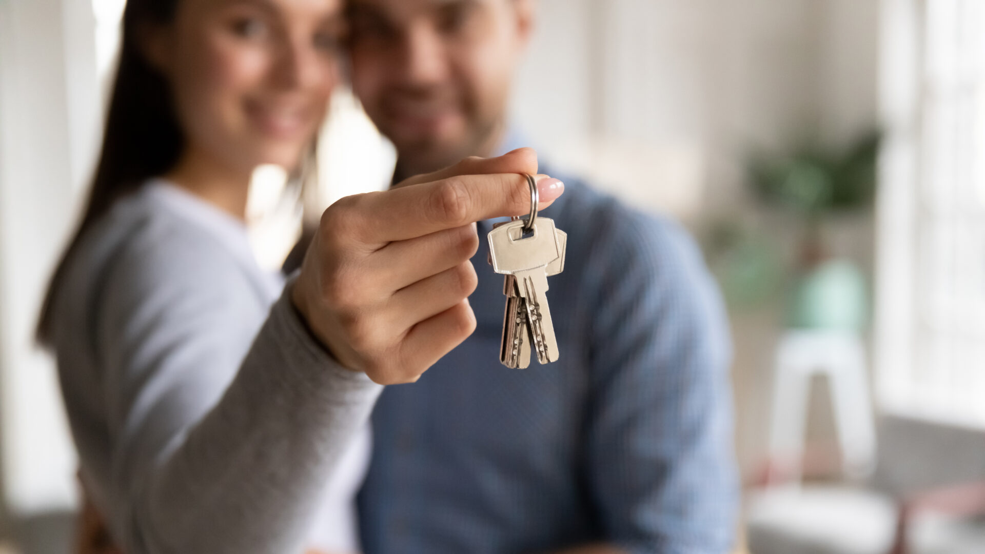 Close up happy woman hugging man, holding keys from new first house, young family celebrating moving day, satisfied customers couple purchase real estate, mortgage and relocation concept