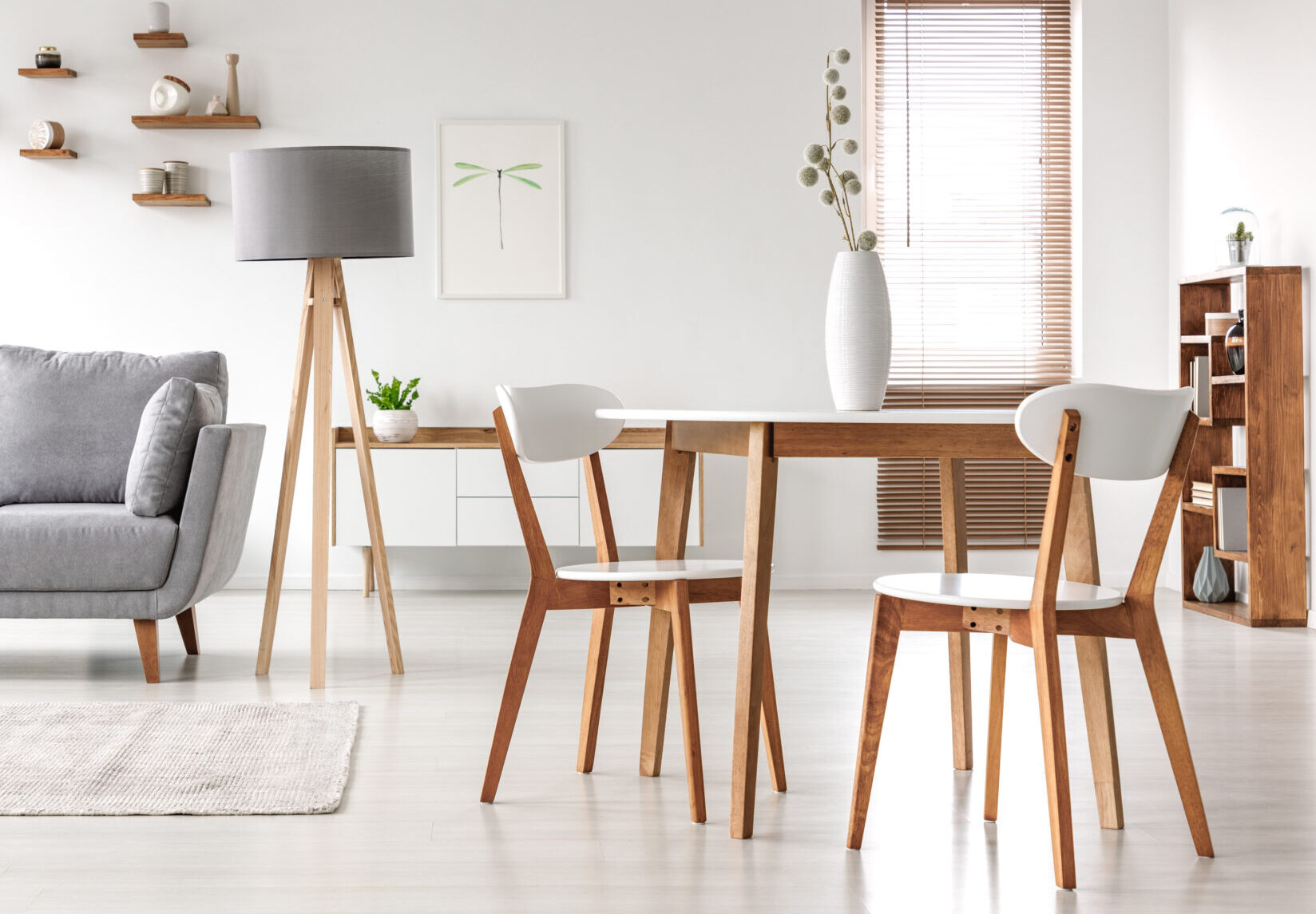 Wooden chairs at table in bright open space interior with lamp next to grey couch