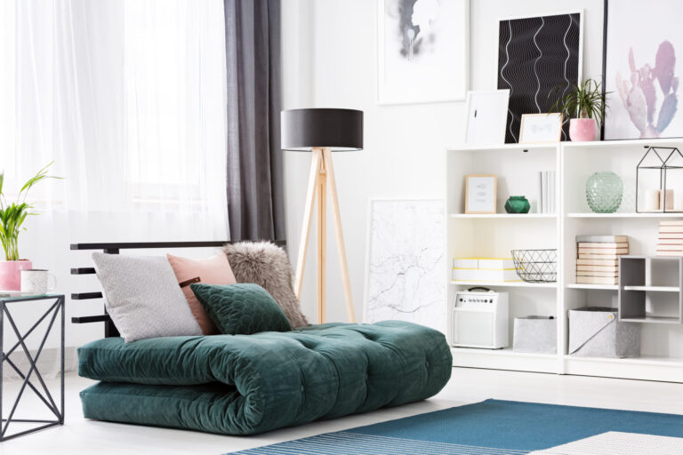 Cushions on green futon in modern bedroom interior with black wooden lamp and posters