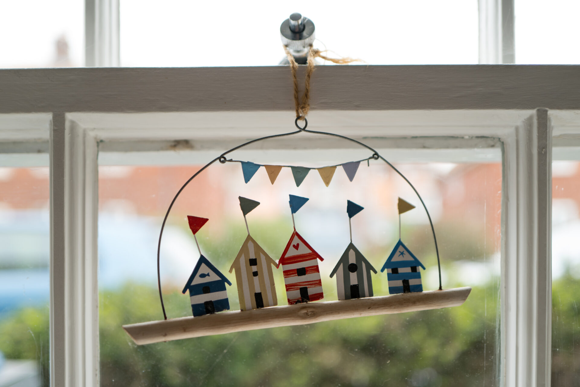 Shallow focus of a home-made wooden beach hut ornament seen hanging on a sash window for a seaside holiday let.